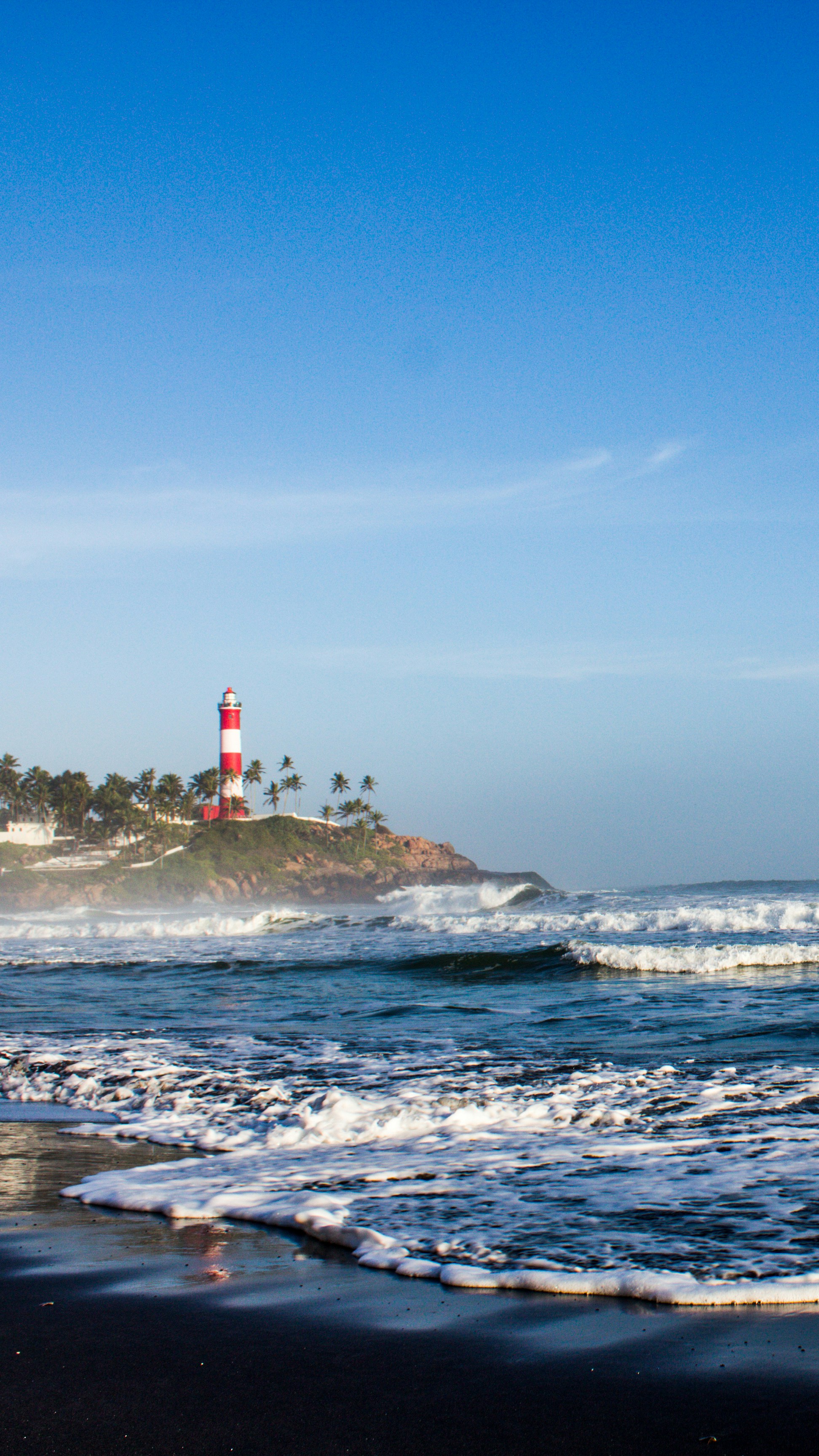 A red-and-white lighthouse rises above the waves at Kovalam Beach.