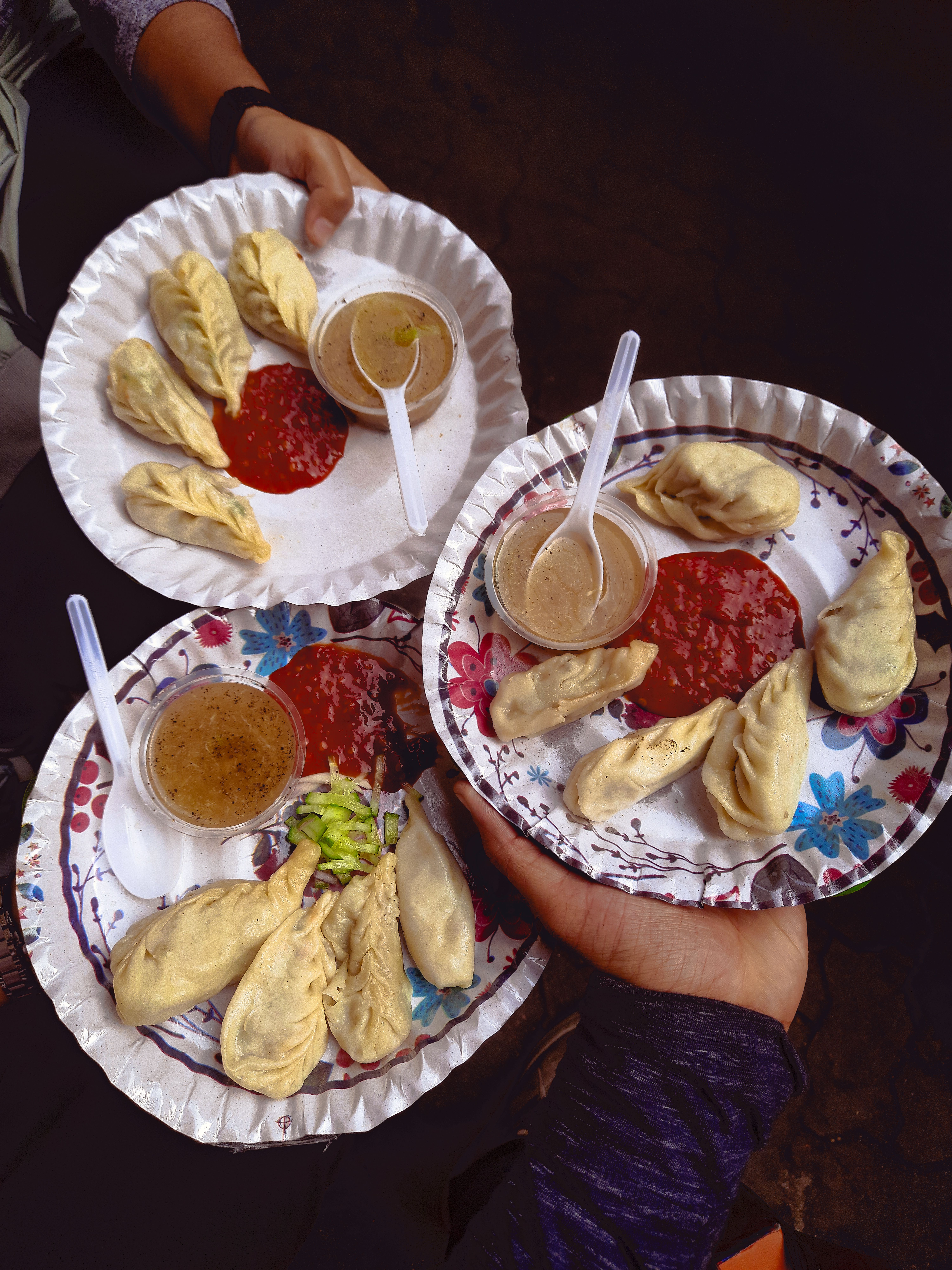 Hands holding plates of steamed momos with chutney, a classic Ladakhi meal