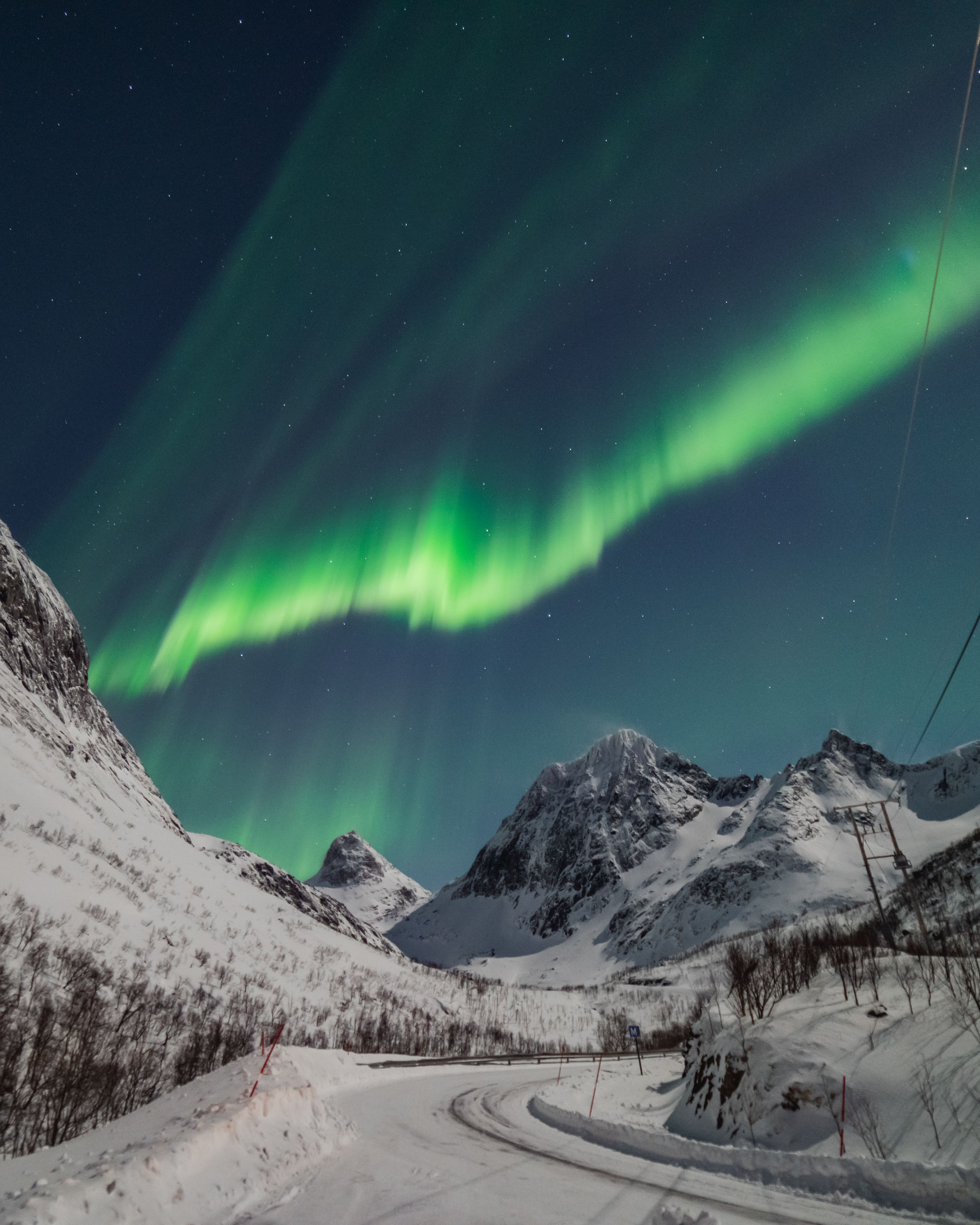 Northern Lights above snow-covered mountains and a winter road near Tromsø