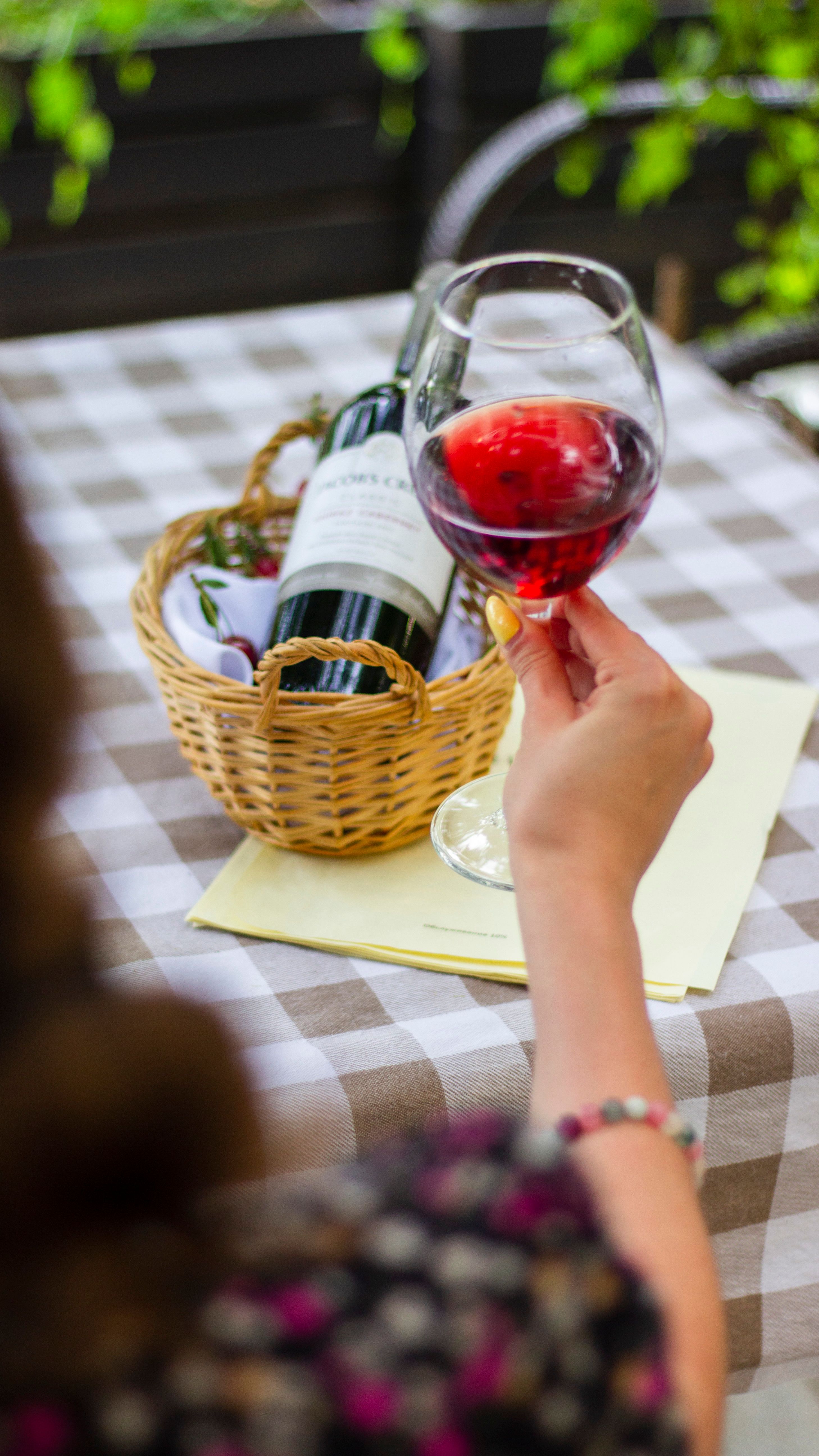 A glass of red wine beside a wine bottle in a basket