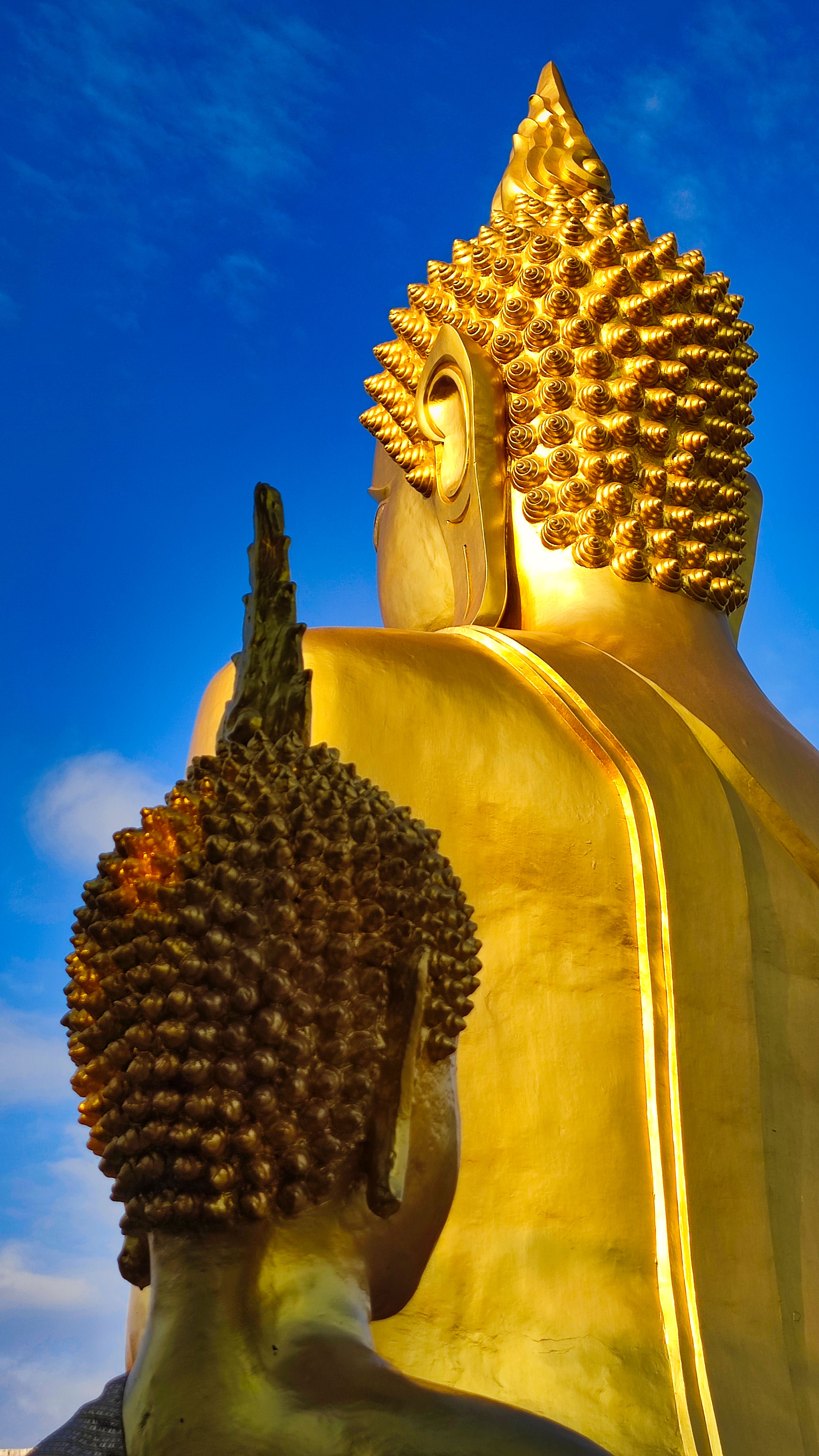 A golden Buddha statue viewed from behind against a blue sky.