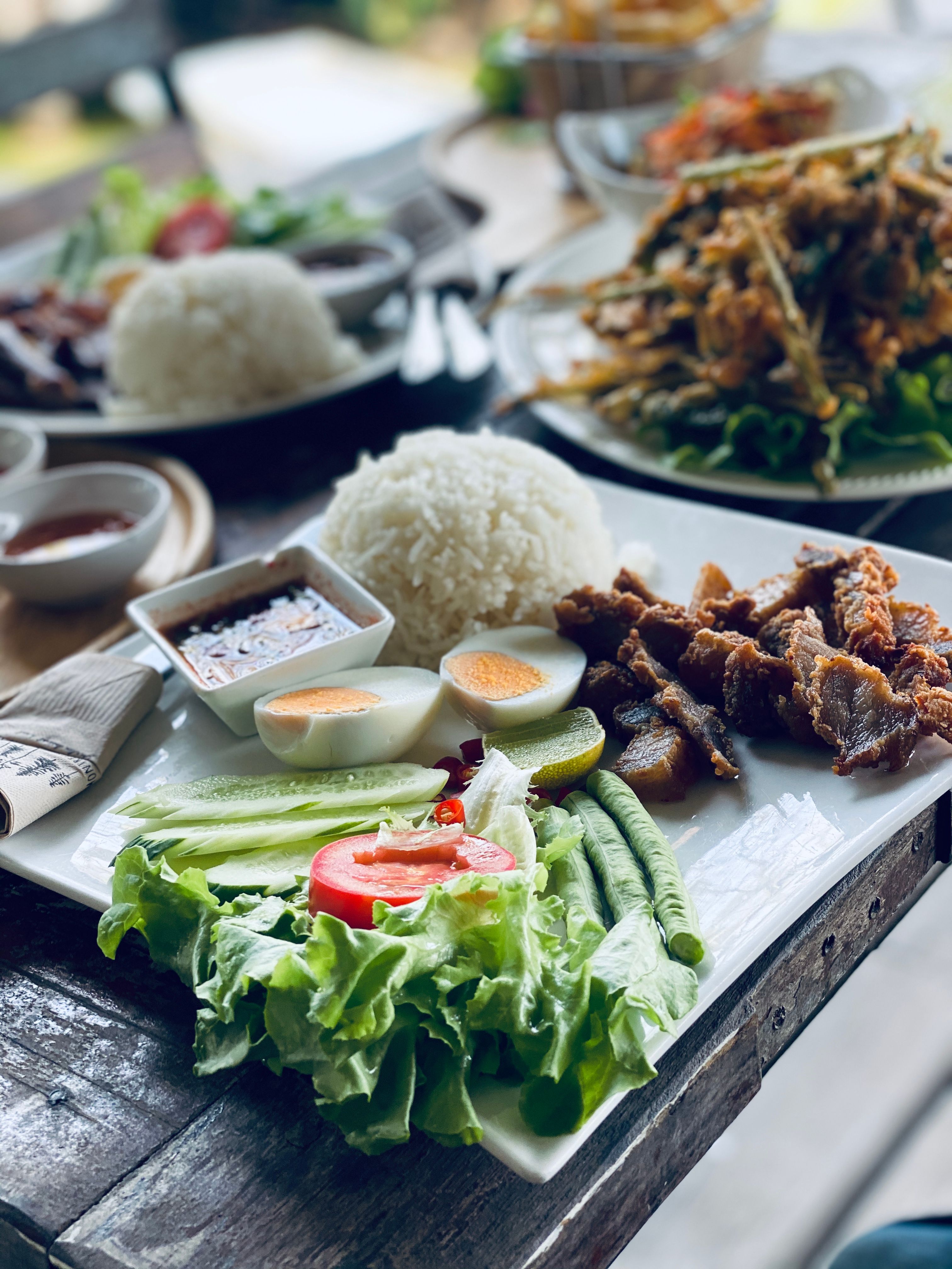 Rice, vegetables and fried food arranged on a plate with dipping sauce.