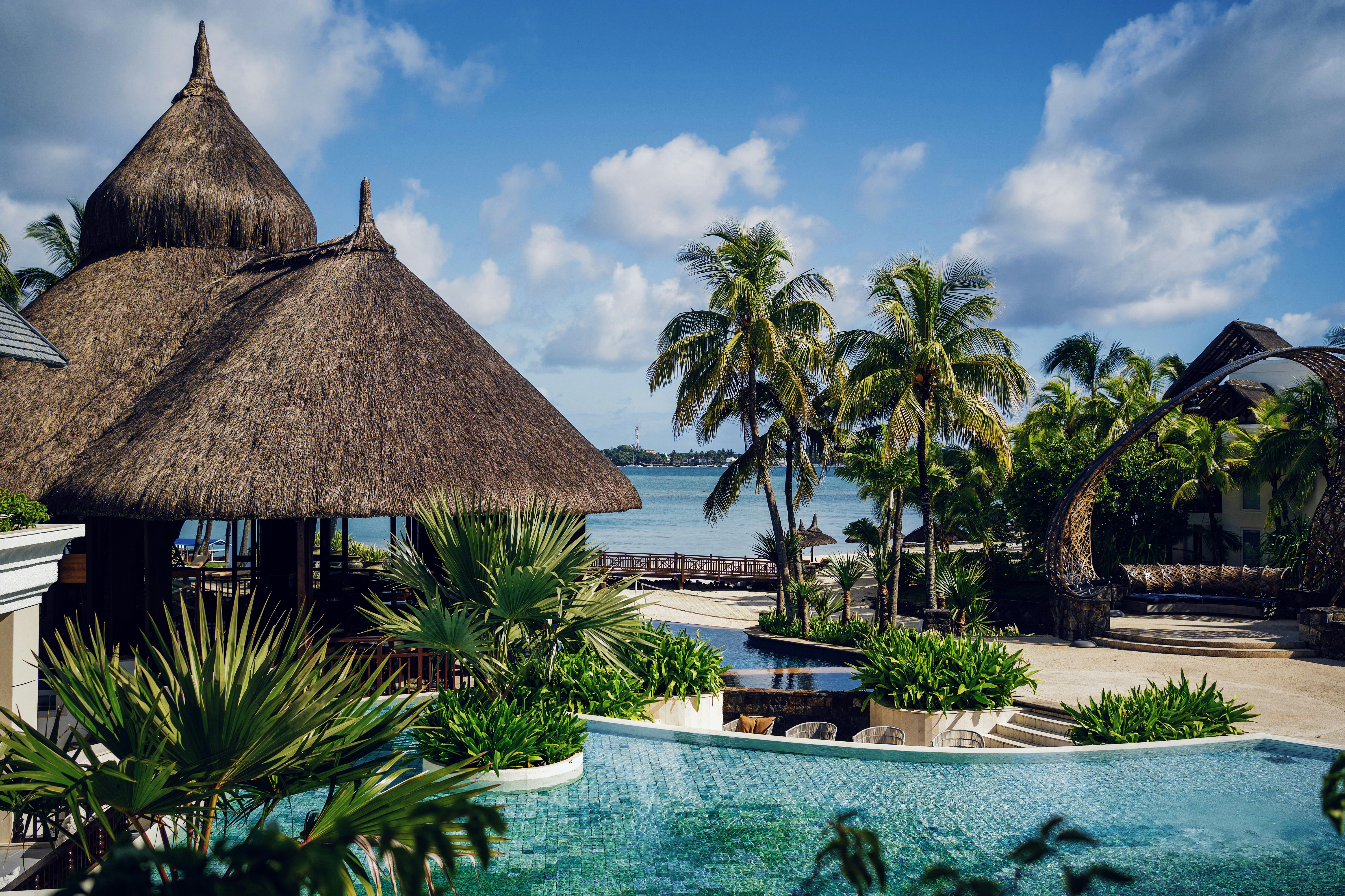 Palm-lined pool and thatched pavilion beside a turquoise lagoon