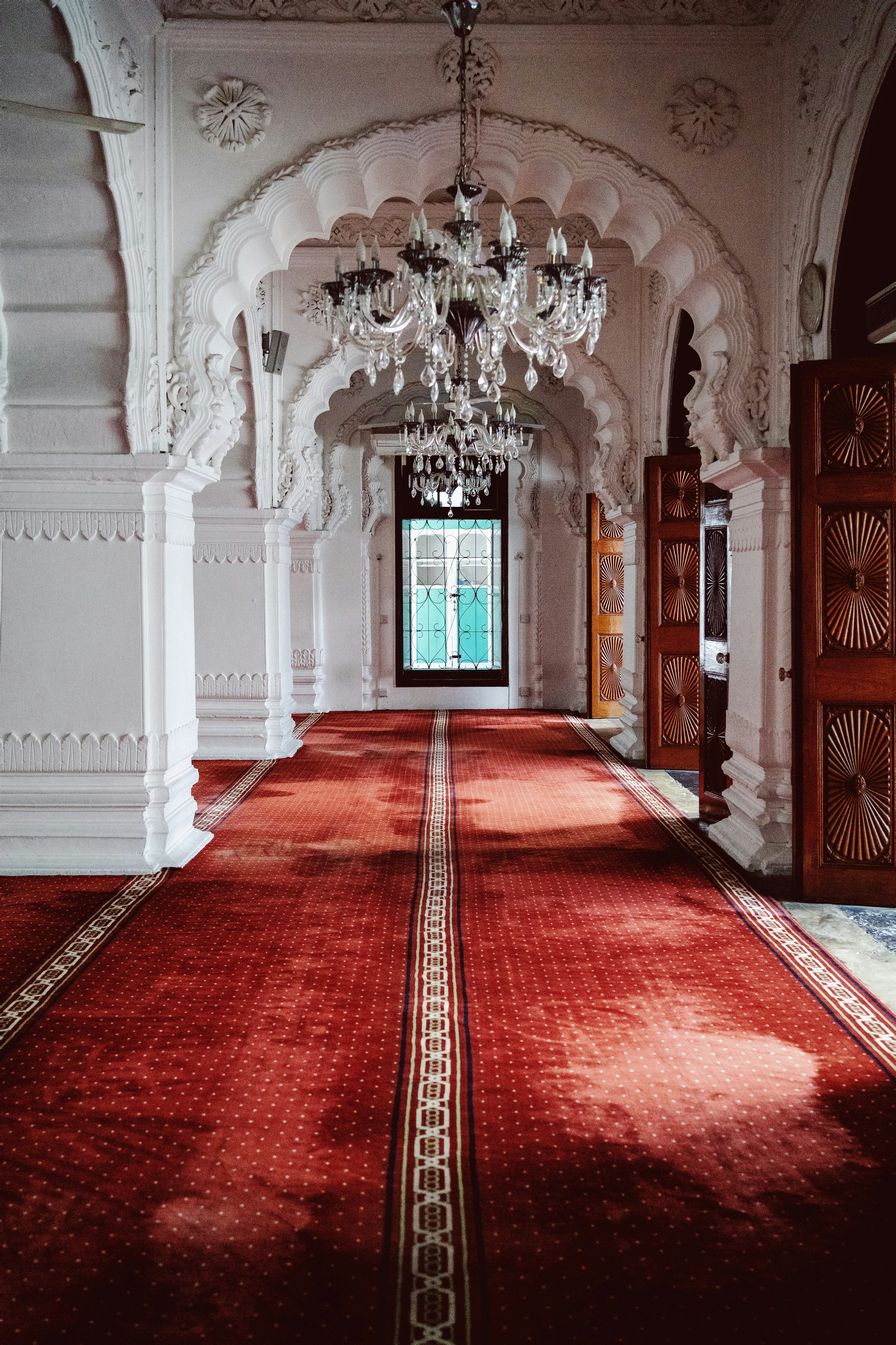 Ornate hall with carved columns, a red carpet and chandeliers