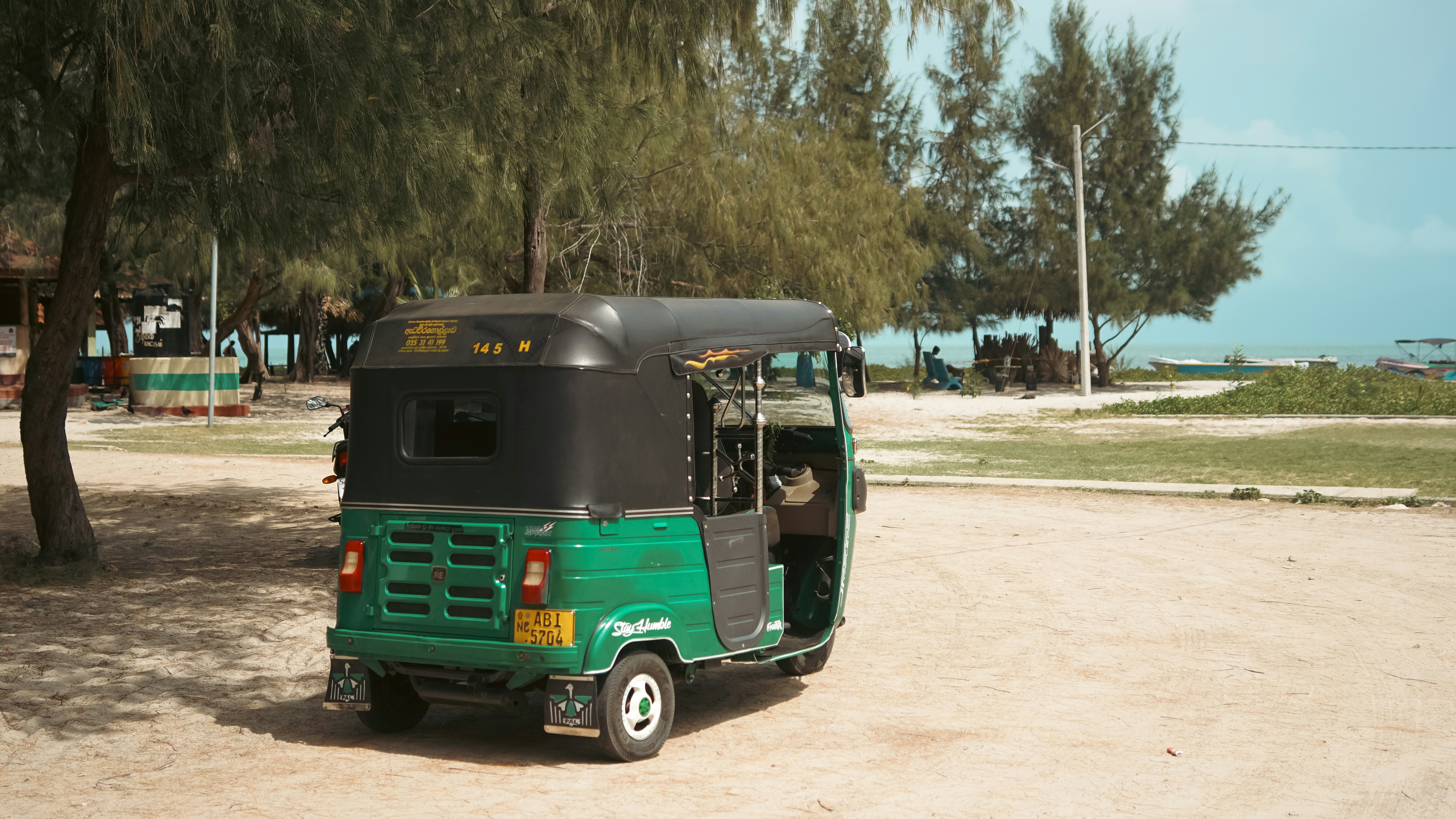 Green tuk-tuk parked beside a sandy, tree-lined beach