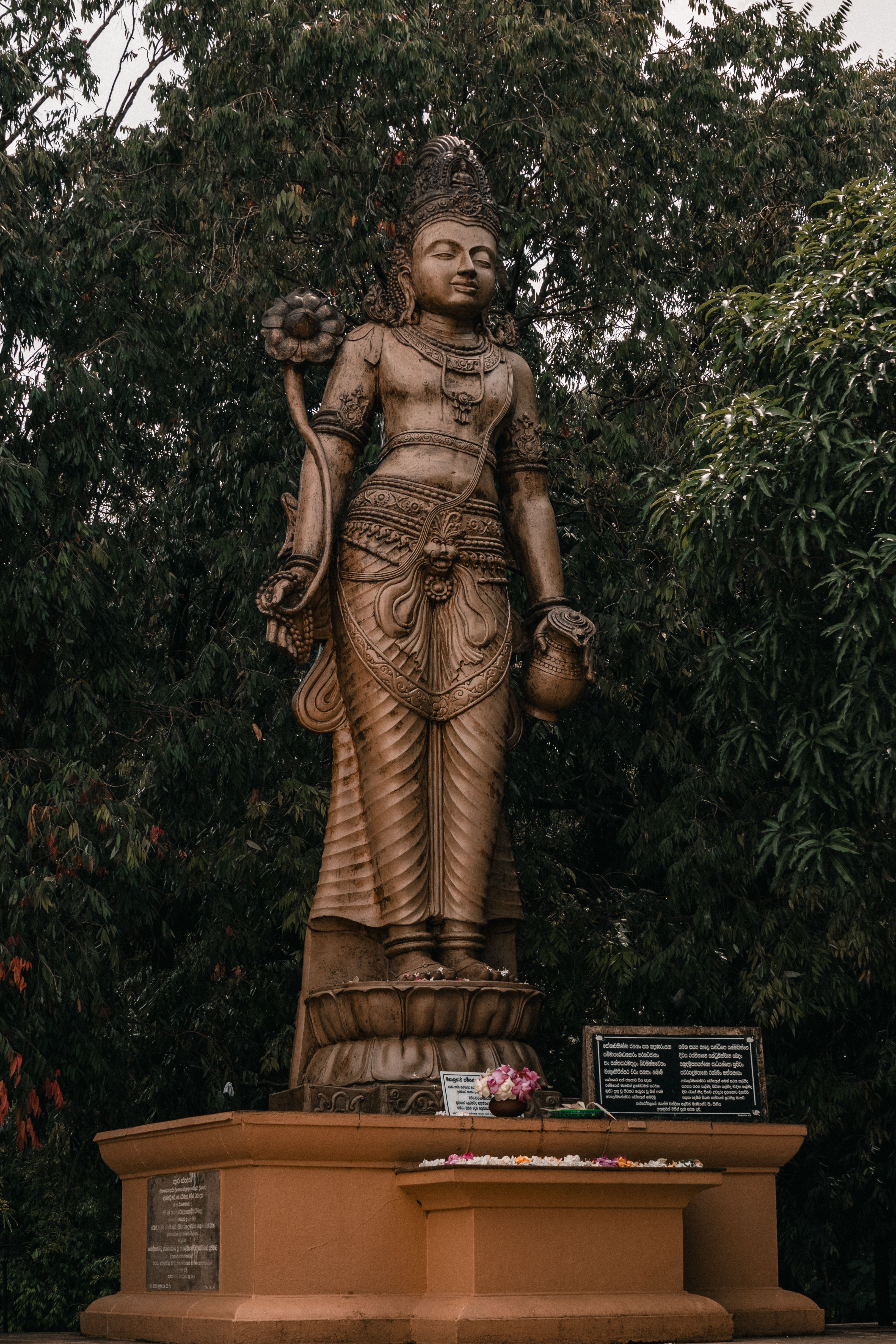 Ornately carved standing figure holding a flower outdoors