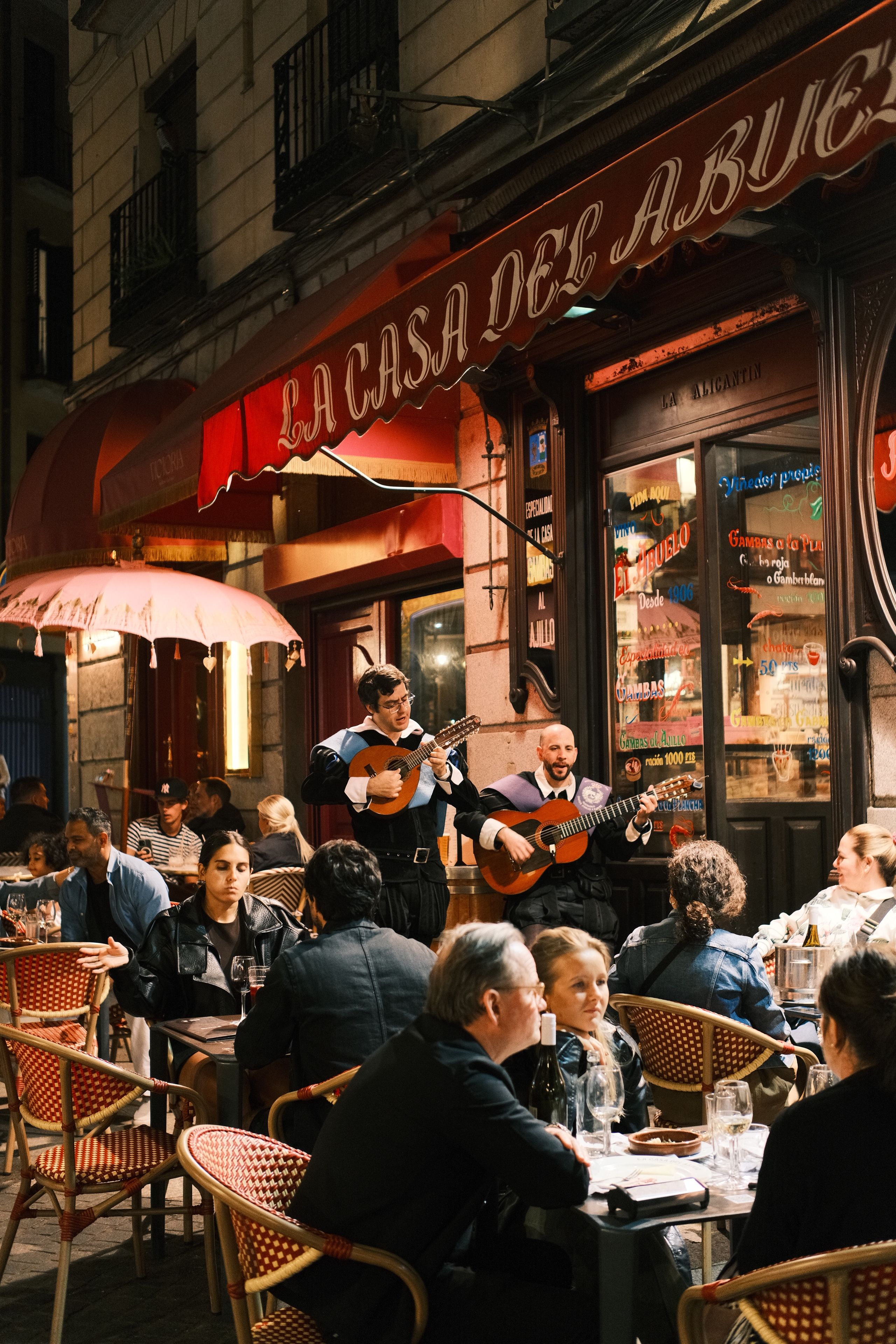 Guitarists perform for diners at an outdoor restaurant terrace.