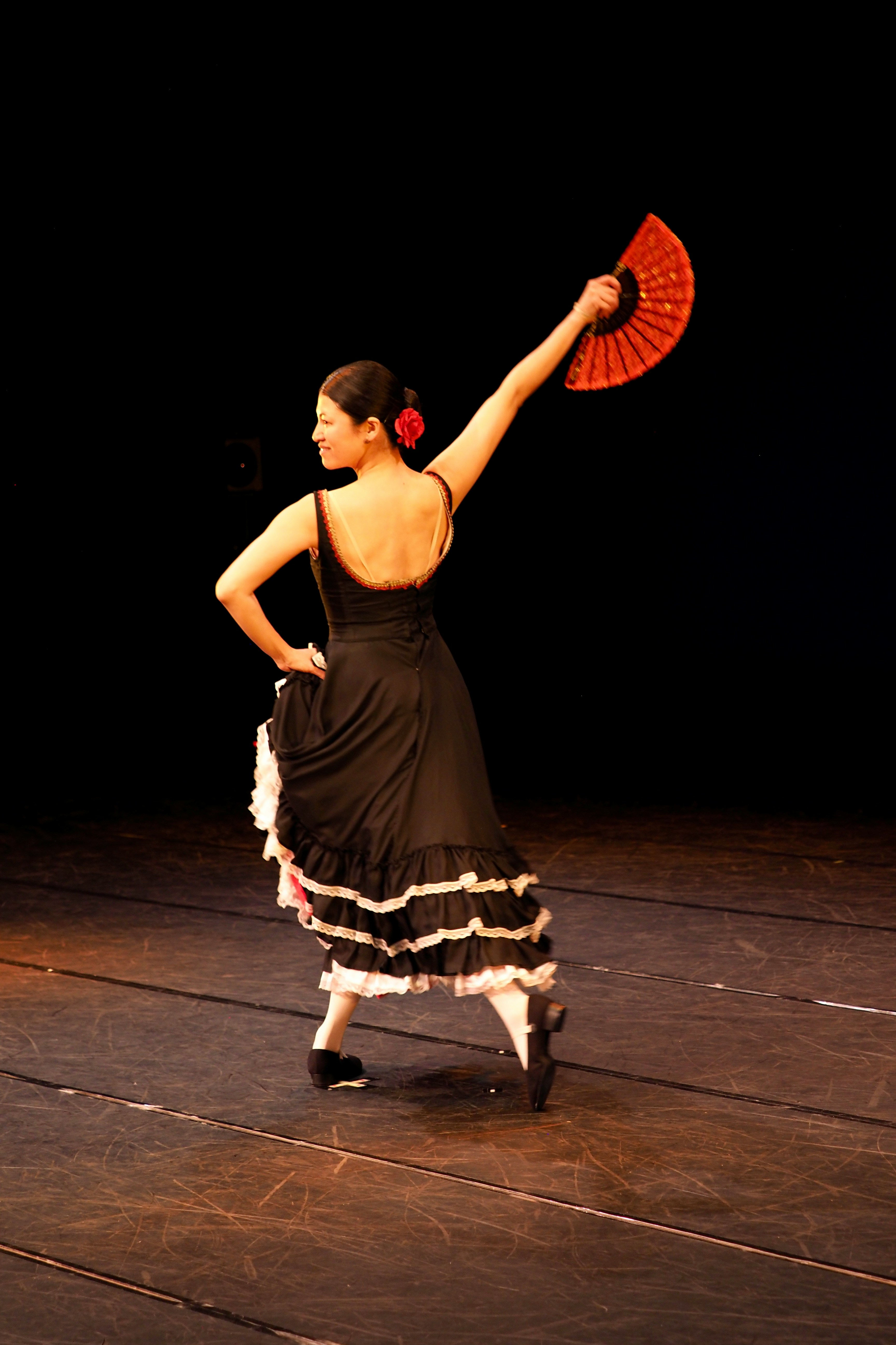 A flamenco dancer performs with a red fan onstage.