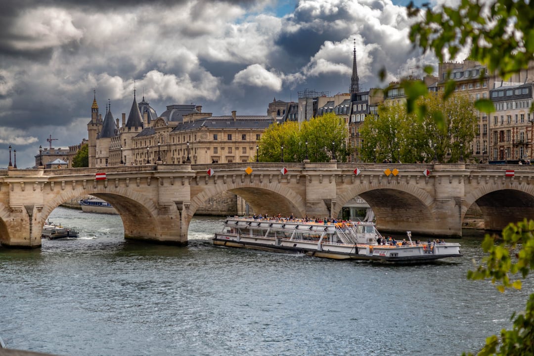 A river cruise boat passing beneath a stone bridge on the Seine in Paris