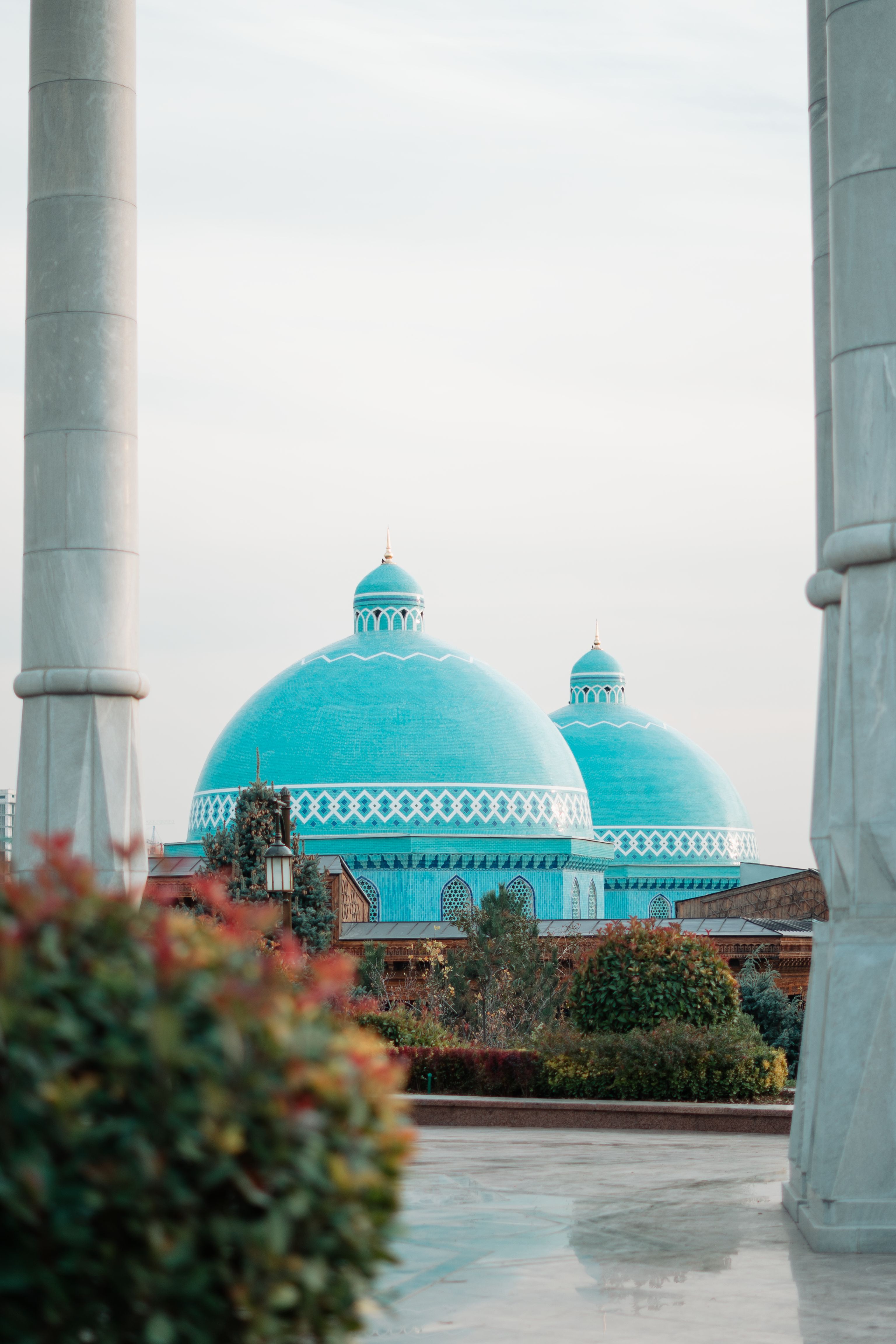 Turquoise domes rise above a Tashkent mosque courtyard framed by stone columns.