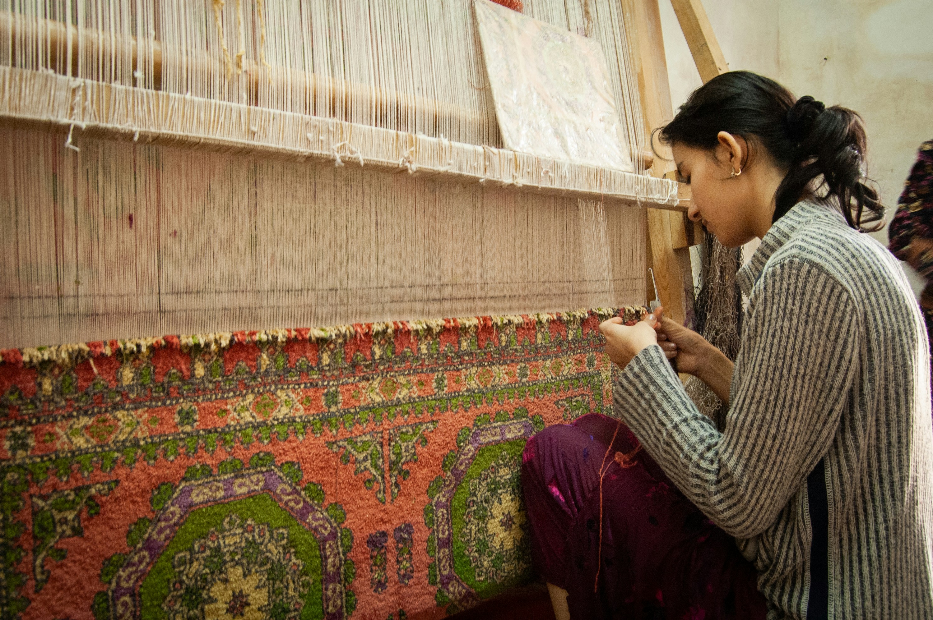 A woman weaving a patterned carpet on a traditional loom.