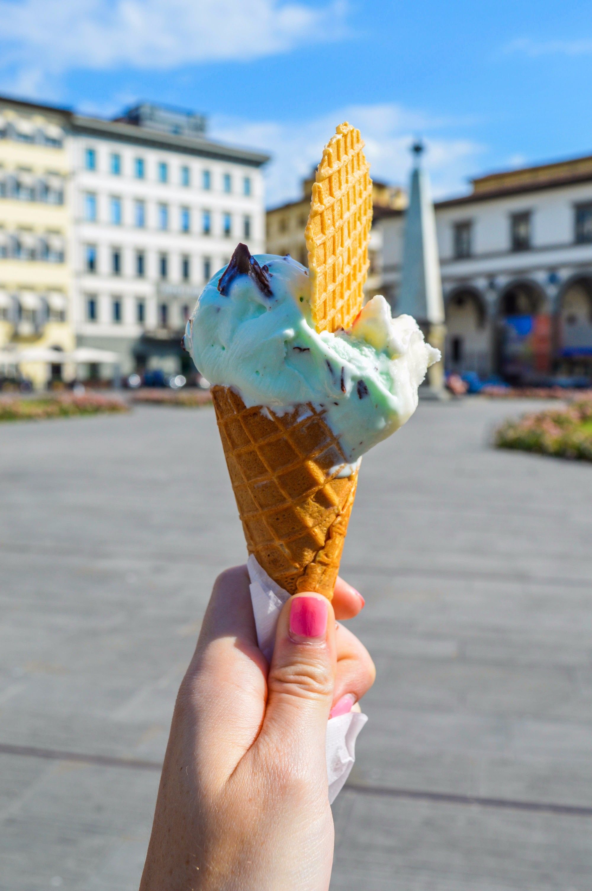 A hand holds a gelato cone against historic buildings in a Florence piazza.